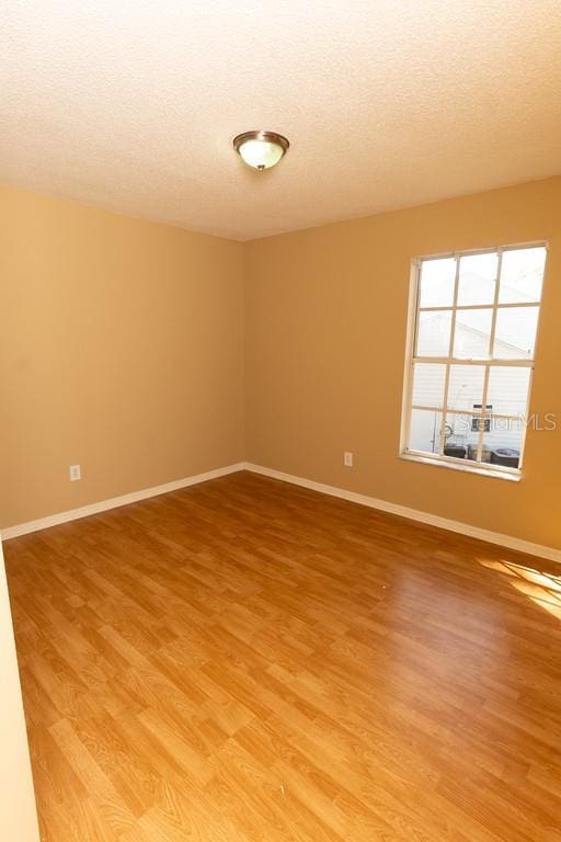 empty room with light wood-style floors, baseboards, and a textured ceiling