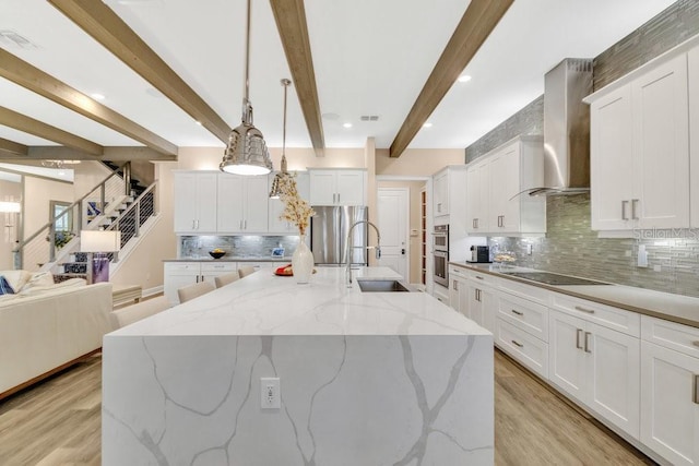 kitchen with wall chimney range hood, light wood-style floors, stainless steel appliances, and a sink