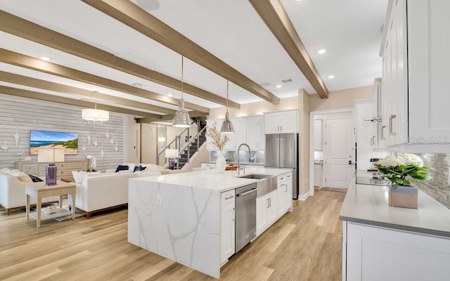 kitchen with appliances with stainless steel finishes, light wood-style floors, open floor plan, white cabinets, and a sink