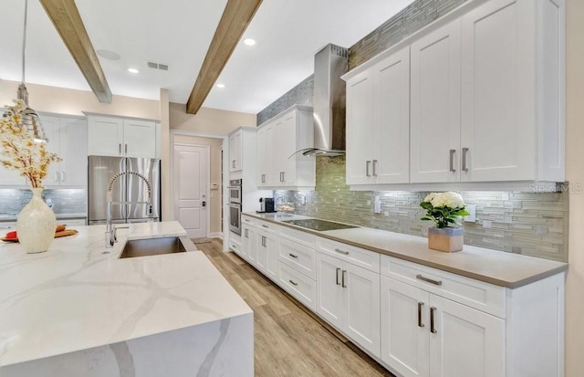 kitchen with visible vents, appliances with stainless steel finishes, a sink, wall chimney range hood, and beamed ceiling