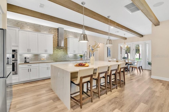 kitchen featuring wall chimney exhaust hood, backsplash, visible vents, and white cabinets