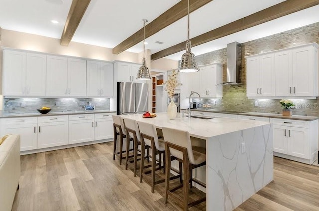 kitchen with a breakfast bar area, a sink, white cabinets, freestanding refrigerator, and wall chimney exhaust hood