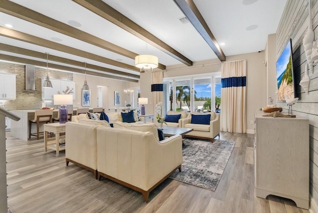 living area with light wood-style floors, a chandelier, and beamed ceiling