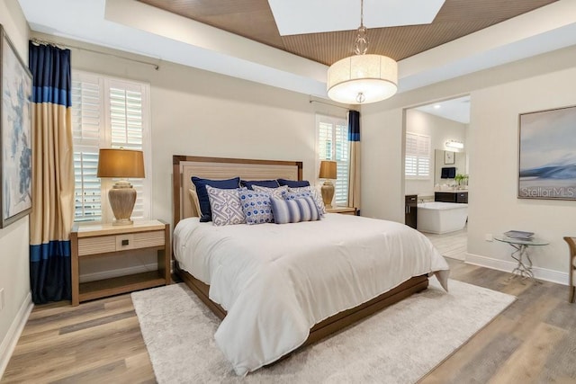 bedroom with a tray ceiling, ensuite bathroom, baseboards, and wood finished floors