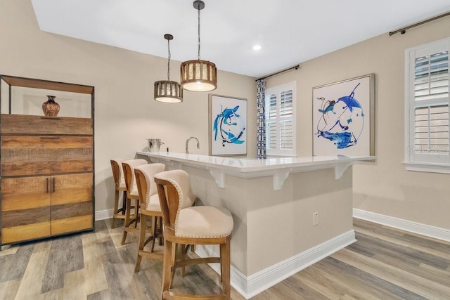 bar featuring indoor wet bar, hanging light fixtures, baseboards, and wood finished floors