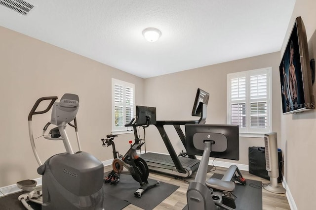 workout room with light wood-style flooring, a textured ceiling, visible vents, and baseboards