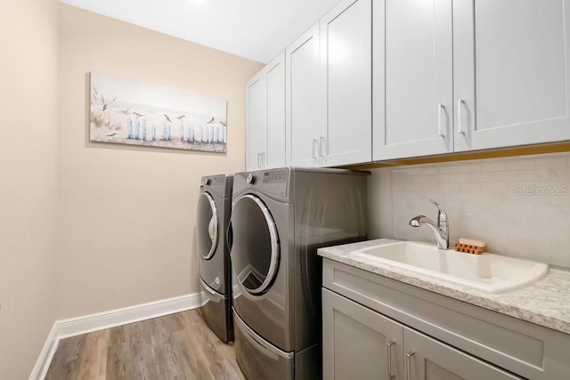 laundry area featuring cabinet space, light wood-style flooring, a sink, independent washer and dryer, and baseboards