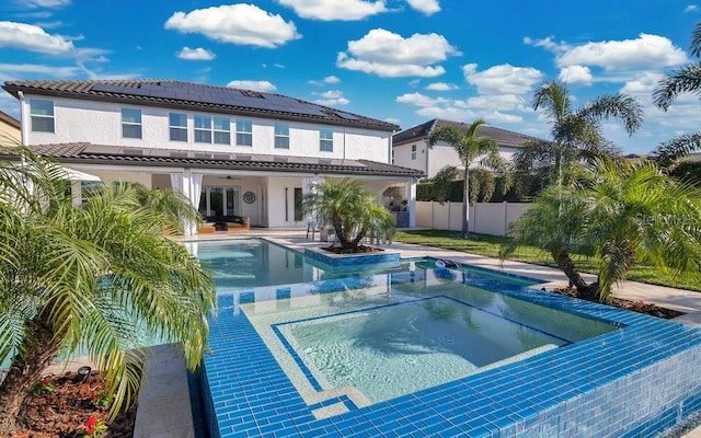 back of house with a ceiling fan, a fenced backyard, an in ground hot tub, roof mounted solar panels, and stucco siding