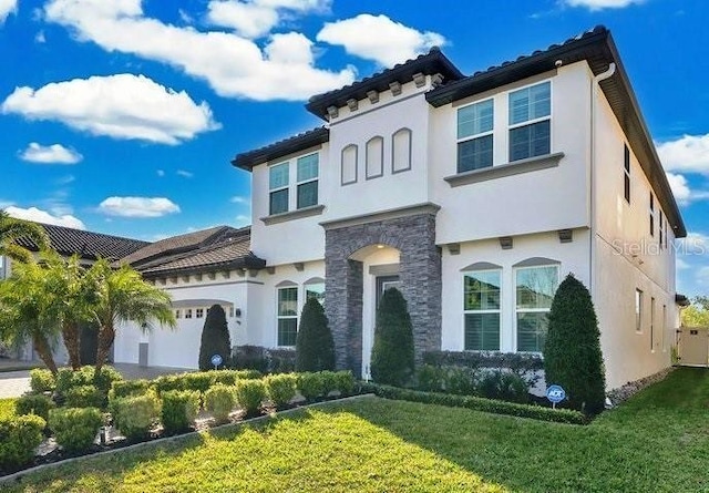 mediterranean / spanish house with an attached garage, stone siding, a front yard, and stucco siding