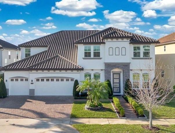 mediterranean / spanish home with a tiled roof, decorative driveway, an attached garage, and stucco siding