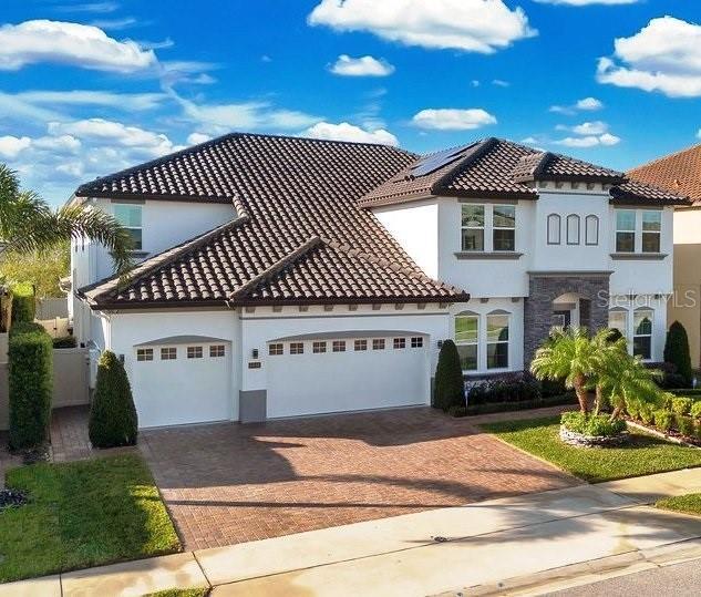 mediterranean / spanish-style house with stone siding, decorative driveway, an attached garage, and stucco siding