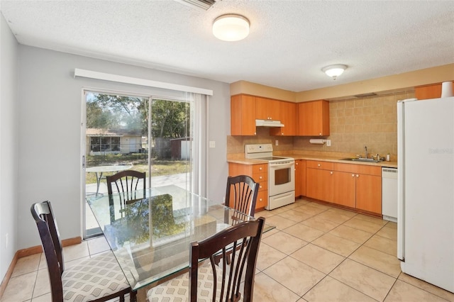 kitchen featuring light countertops, light tile patterned flooring, a sink, white appliances, and under cabinet range hood