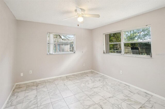 unfurnished room with marble finish floor, ceiling fan, a textured ceiling, and baseboards