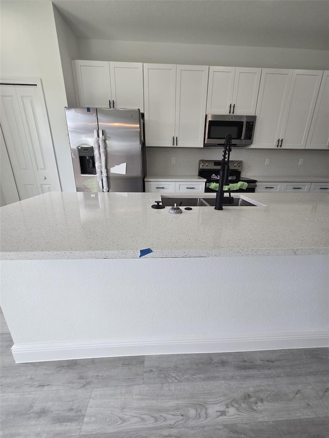 kitchen featuring stainless steel appliances, a sink, white cabinets, and light stone countertops