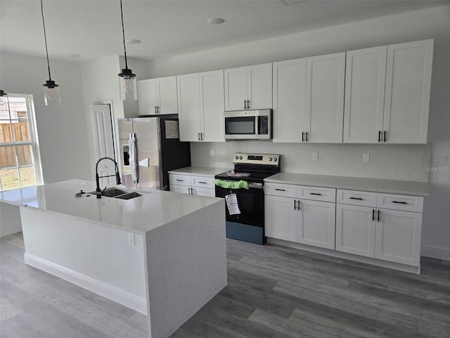 kitchen with appliances with stainless steel finishes, a kitchen island with sink, white cabinets, a sink, and wood finished floors