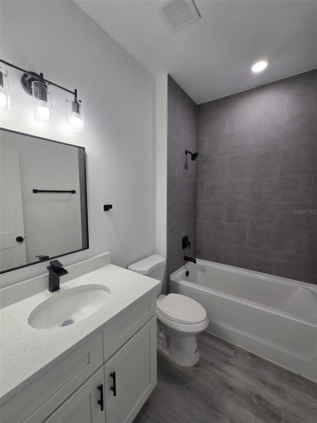 bathroom with visible vents, bathing tub / shower combination, toilet, wood finished floors, and vanity