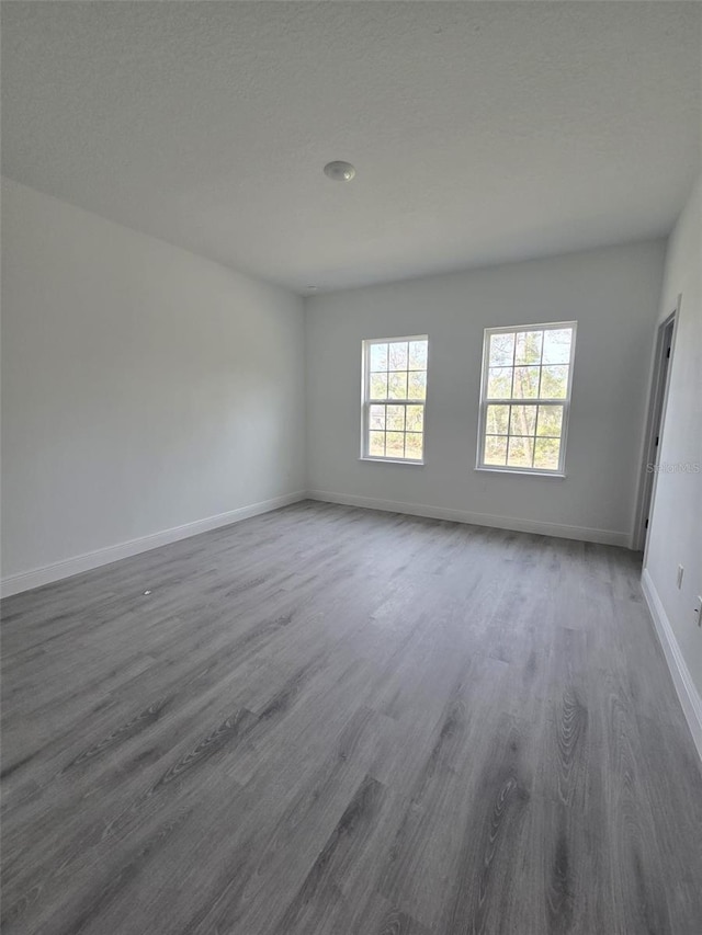 spare room featuring a textured ceiling, wood finished floors, and baseboards