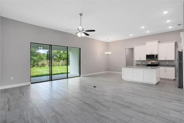 kitchen with ceiling fan with notable chandelier, open floor plan, stainless steel appliances, baseboards, and light stone countertops