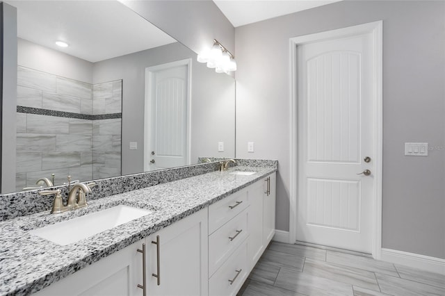 bathroom with a sink, baseboards, double vanity, and a tile shower