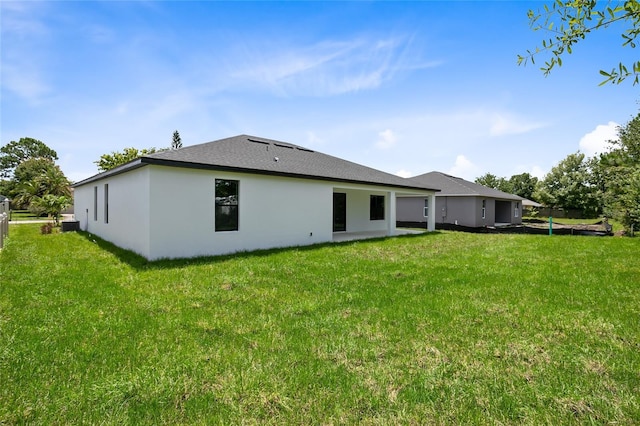 back of property with a lawn, roof with shingles, and stucco siding