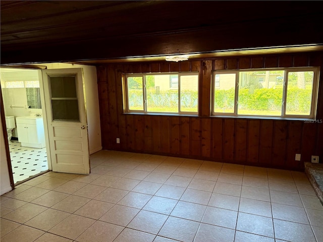 unfurnished room featuring light tile patterned floors, plenty of natural light, and wooden walls