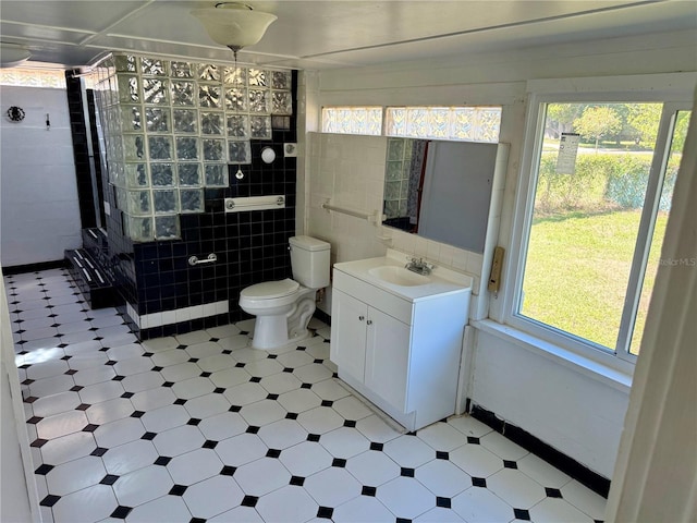 bathroom with tile patterned floors, toilet, tile walls, tiled shower, and vanity