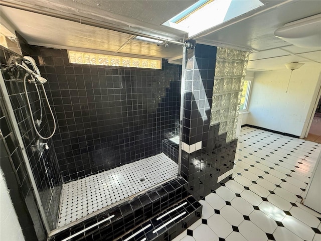 bathroom with tile patterned floors, baseboards, a skylight, and a tile shower