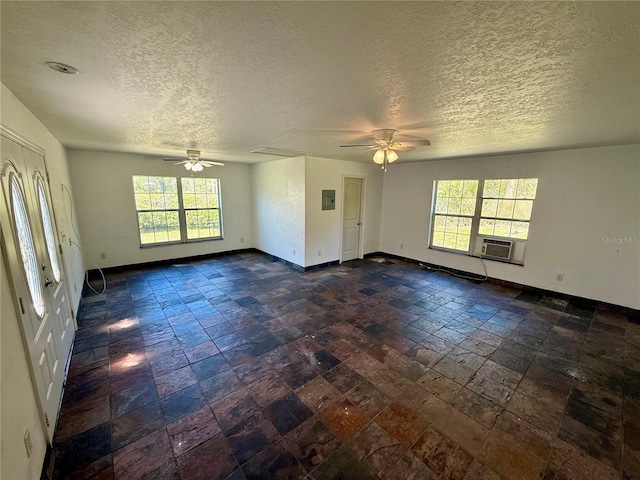 empty room featuring stone tile floors, cooling unit, a ceiling fan, and baseboards