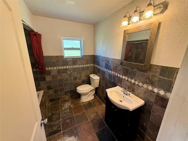 bathroom with a wainscoted wall, toilet, a textured ceiling, tile walls, and vanity