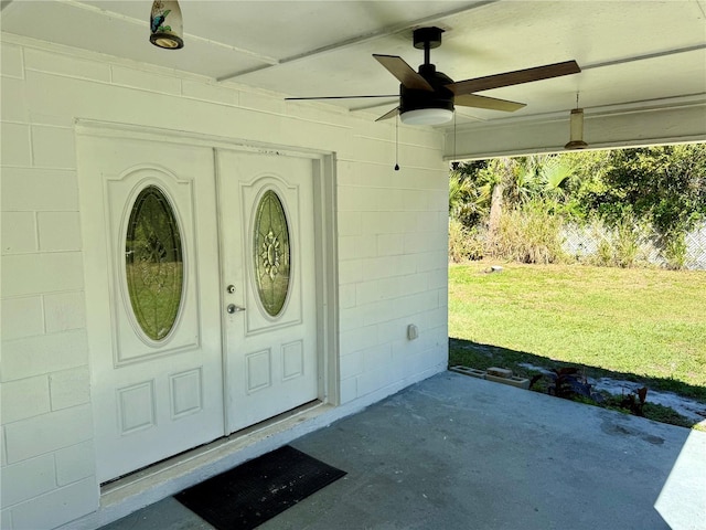 property entrance with a yard, concrete block siding, and a ceiling fan