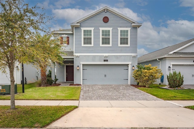 traditional home with an attached garage, decorative driveway, a front yard, and stucco siding