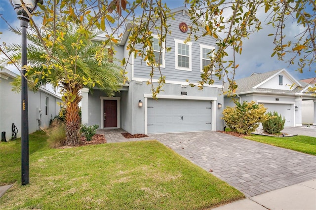 traditional-style house featuring a garage, decorative driveway, a front yard, and stucco siding