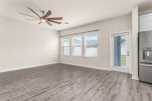 unfurnished room with a ceiling fan, visible vents, baseboards, and wood finished floors