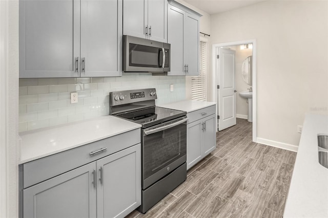 kitchen featuring light wood-style floors, tasteful backsplash, stainless steel appliances, and light countertops