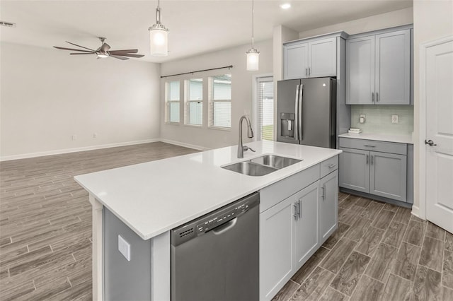 kitchen featuring appliances with stainless steel finishes, open floor plan, a sink, and gray cabinetry