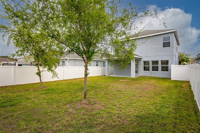 rear view of house featuring a fenced backyard, a yard, and stucco siding