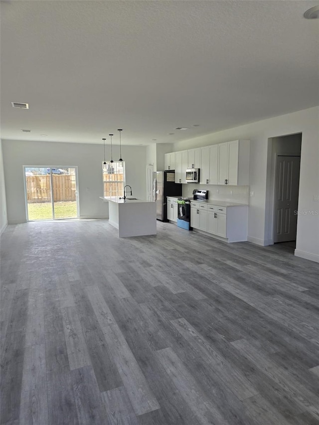 unfurnished living room with a textured ceiling, dark wood-type flooring, a sink, visible vents, and baseboards