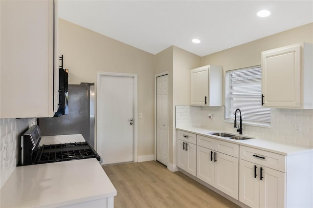 kitchen featuring light countertops, light wood-style floors, white cabinets, a sink, and gas range