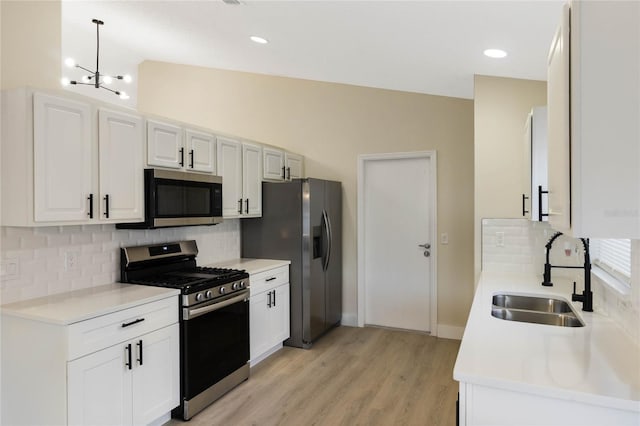 kitchen with stainless steel appliances, light countertops, white cabinetry, a sink, and light wood-type flooring