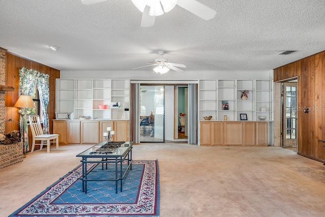 living area with visible vents, a textured ceiling, wood walls, light colored carpet, and ceiling fan