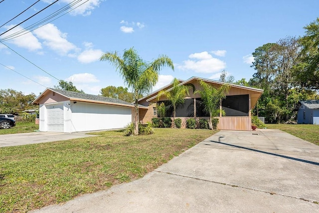 mid-century inspired home with concrete driveway, a sunroom, a front yard, and an outdoor structure