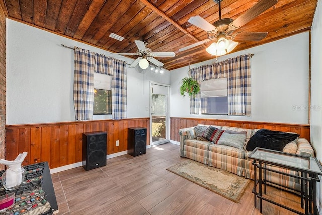 living area featuring wainscoting, wooden ceiling, wooden walls, and a ceiling fan