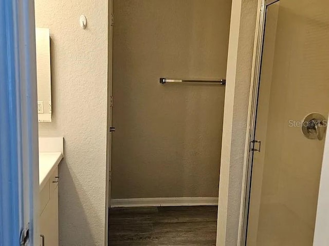 bathroom featuring a stall shower, baseboards, a textured wall, wood finished floors, and vanity