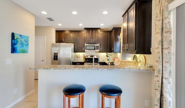 kitchen featuring visible vents, dark brown cabinets, light stone countertops, a peninsula, and stainless steel appliances