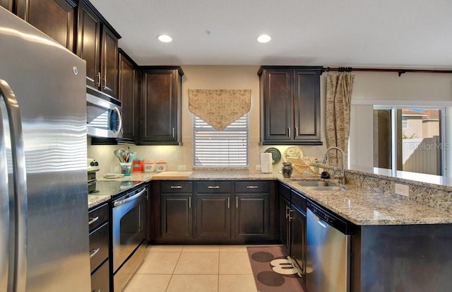 kitchen with light stone countertops, dark brown cabinetry, appliances with stainless steel finishes, light tile patterned flooring, and a sink