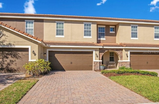 view of property with a tiled roof, decorative driveway, stone siding, and stucco siding