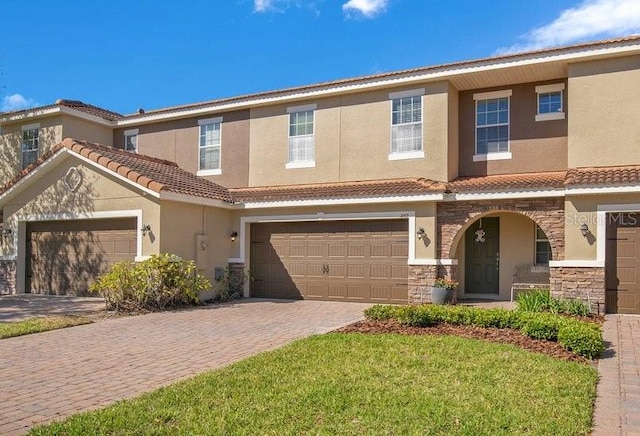 multi unit property with stucco siding, a tile roof, decorative driveway, stone siding, and an attached garage