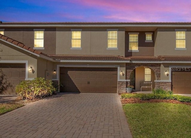 multi unit property with decorative driveway, stone siding, an attached garage, and stucco siding