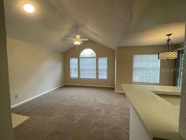 unfurnished living room featuring baseboards, lofted ceiling, ceiling fan, a textured ceiling, and carpet flooring