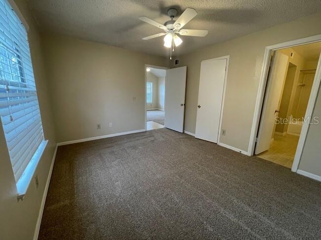 unfurnished bedroom featuring a ceiling fan, carpet flooring, a textured ceiling, ensuite bath, and baseboards